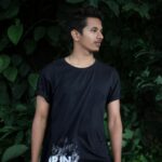 A young man poses casually outdoors against lush greenery in Bengaluru, India.